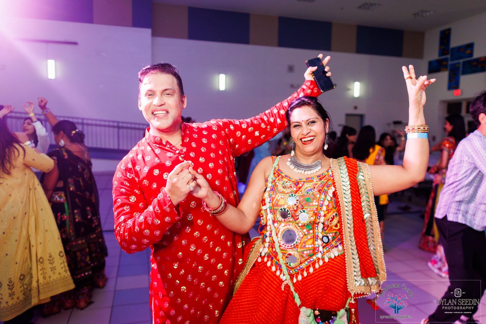 A couple in red and orange outfits laughing and dancing in purple light