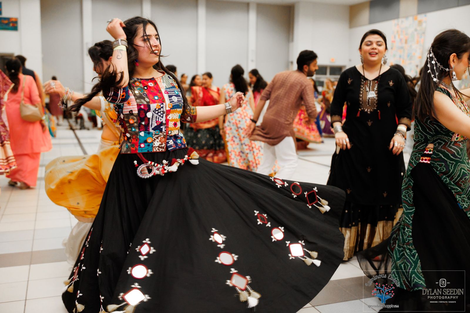 A dancer twirling in a black mirror-work lehenga while others dance around her